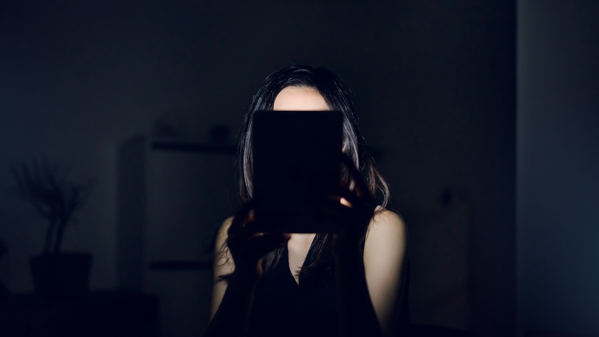 A woman, facing the camera, has her face hidden behind a device she is holding.