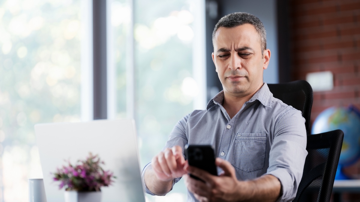 A man sitting at his desk is annoyed about a phone call he is receiving before answering it