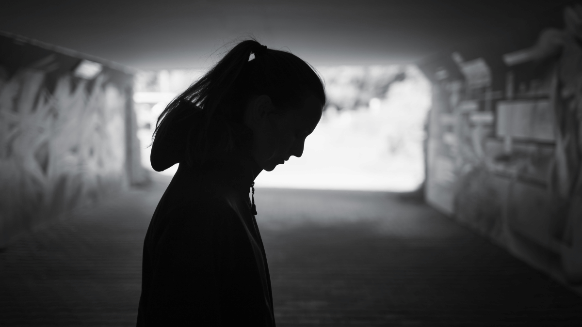 Silhouette of woman in underpass looking down at the ground