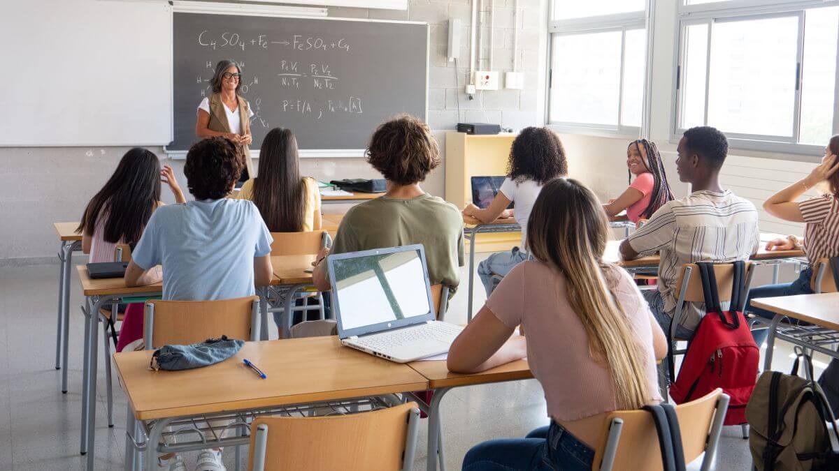 A group of students looking toward a teacher at the front of a classroom