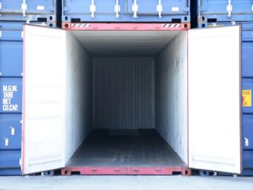 A cargo container is opened up amidst other containers. It is entirely empty.