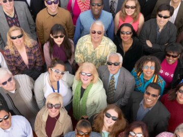 A group of people wearing a variety of sunglasses looking up at the sky and into the camera