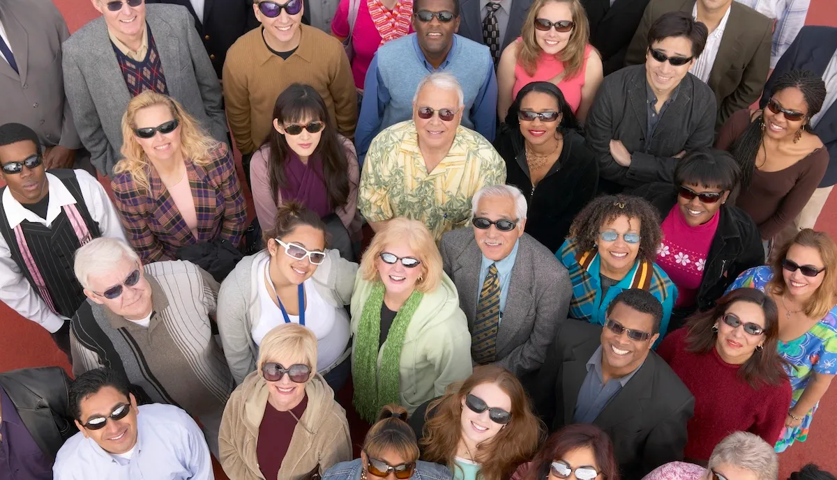 A group of people wearing a variety of sunglasses looking up at the sky and into the camera