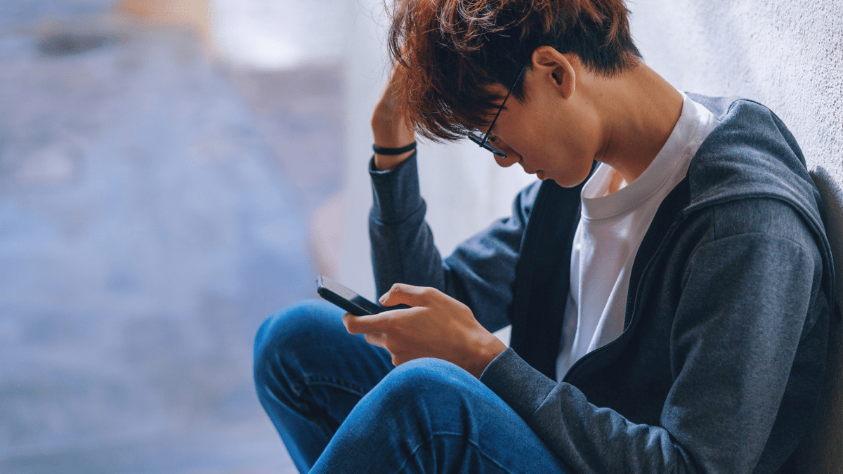 A young man sat down with his head in one hand and holding a phone in the other.