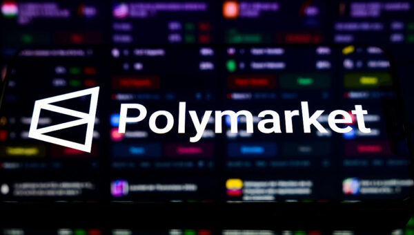 The Polymarket prediction market platform logo appears on a smartphone placed on a reflective surface onto which a list of available bets is projected.