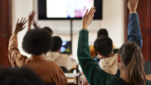Students with hands raised in classroom.