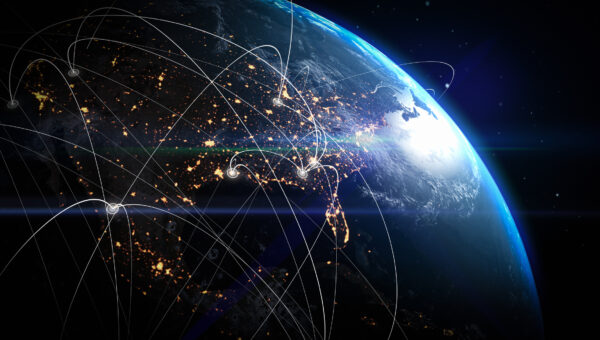 View of Earth from space at night showing illuminated city lights and glowing data network lines connecting various points across continents, symbolizing global communication, technology, and interconnected digital infrastructure.