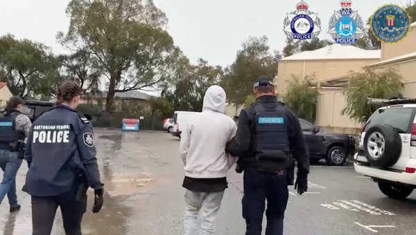 a photo of australian police walking with one of the alleged TeamPCP hackers in handcuffs